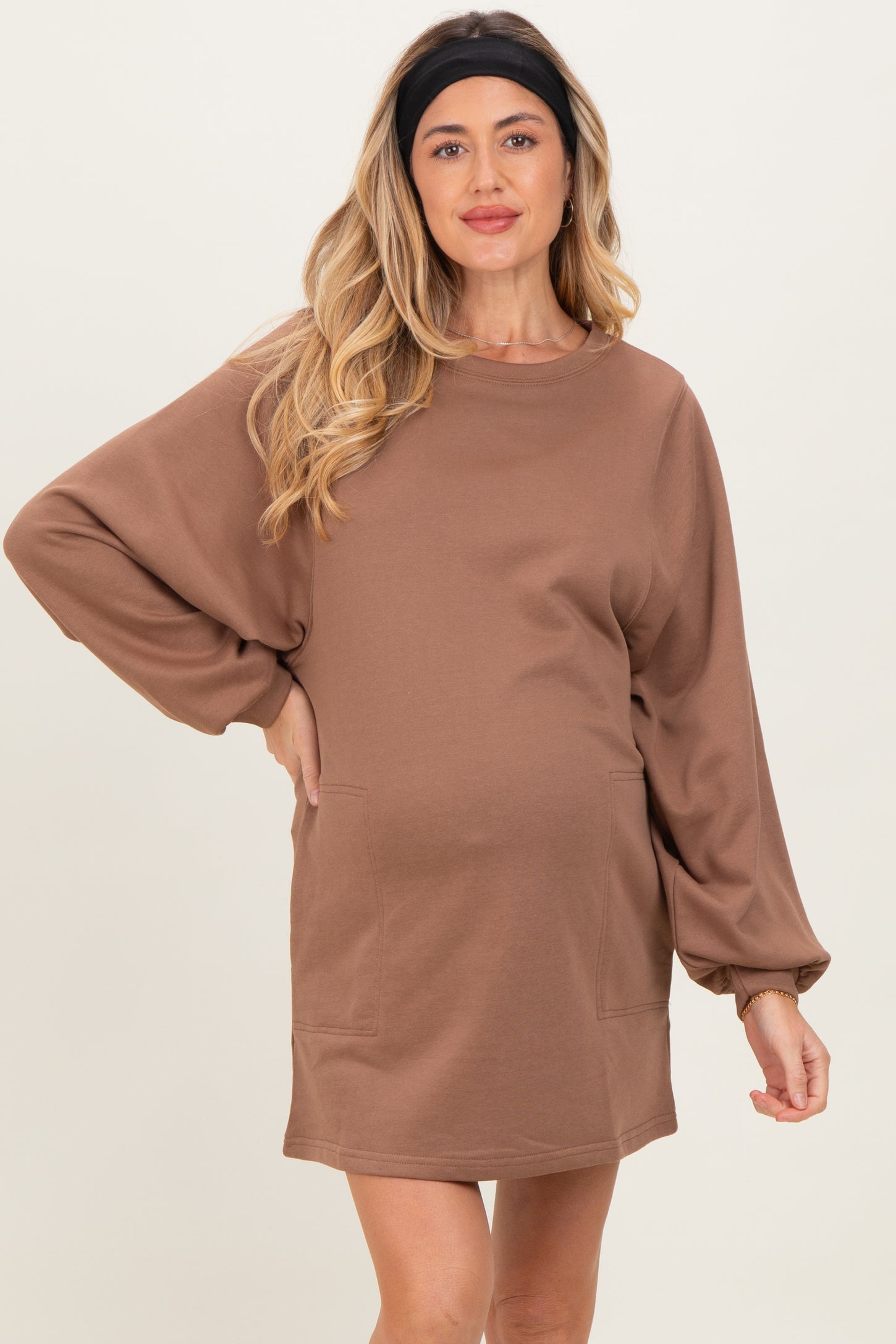 woman wearing a brown long sleeve maternity dress with side pockets and a relaxed fit, showing her baby bump