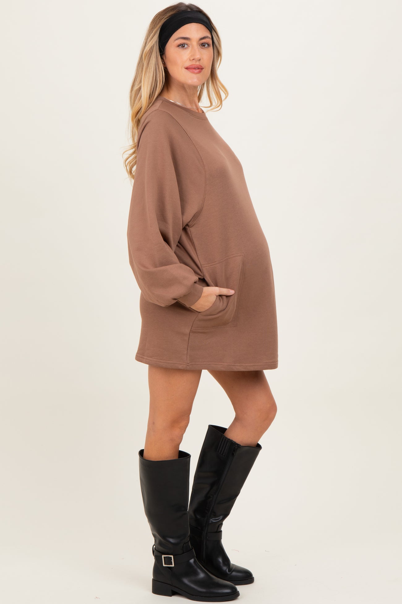woman wearing a chocolate brown maternity sweatshirt dress with long sleeves and a front pocket, showing her baby bump