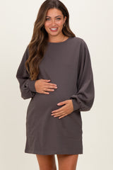 woman wearing a dark grey maternity dress with long sleeves and pockets, holding her baby bump