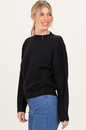 woman wearing a black sweater with cable-knit sleeves and a round neckline paired with high-waisted jeans
