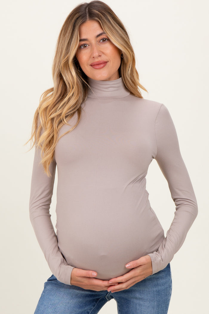 woman wearing a taupe long sleeve maternity top with a fitted turtleneck and holding her baby bump