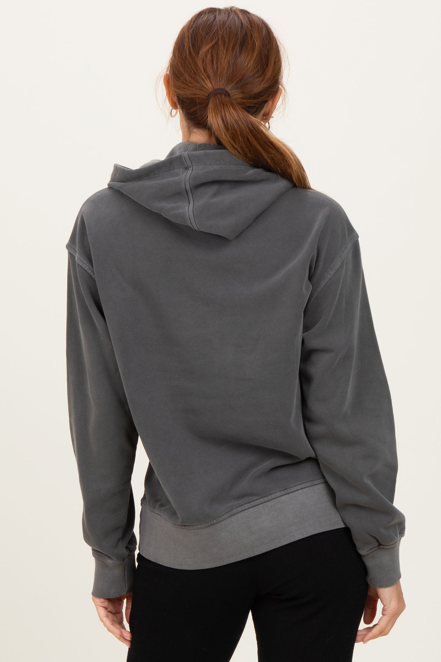 woman wearing a dark gray oversized hoodie with a hood and ribbed hem, shown from the back
