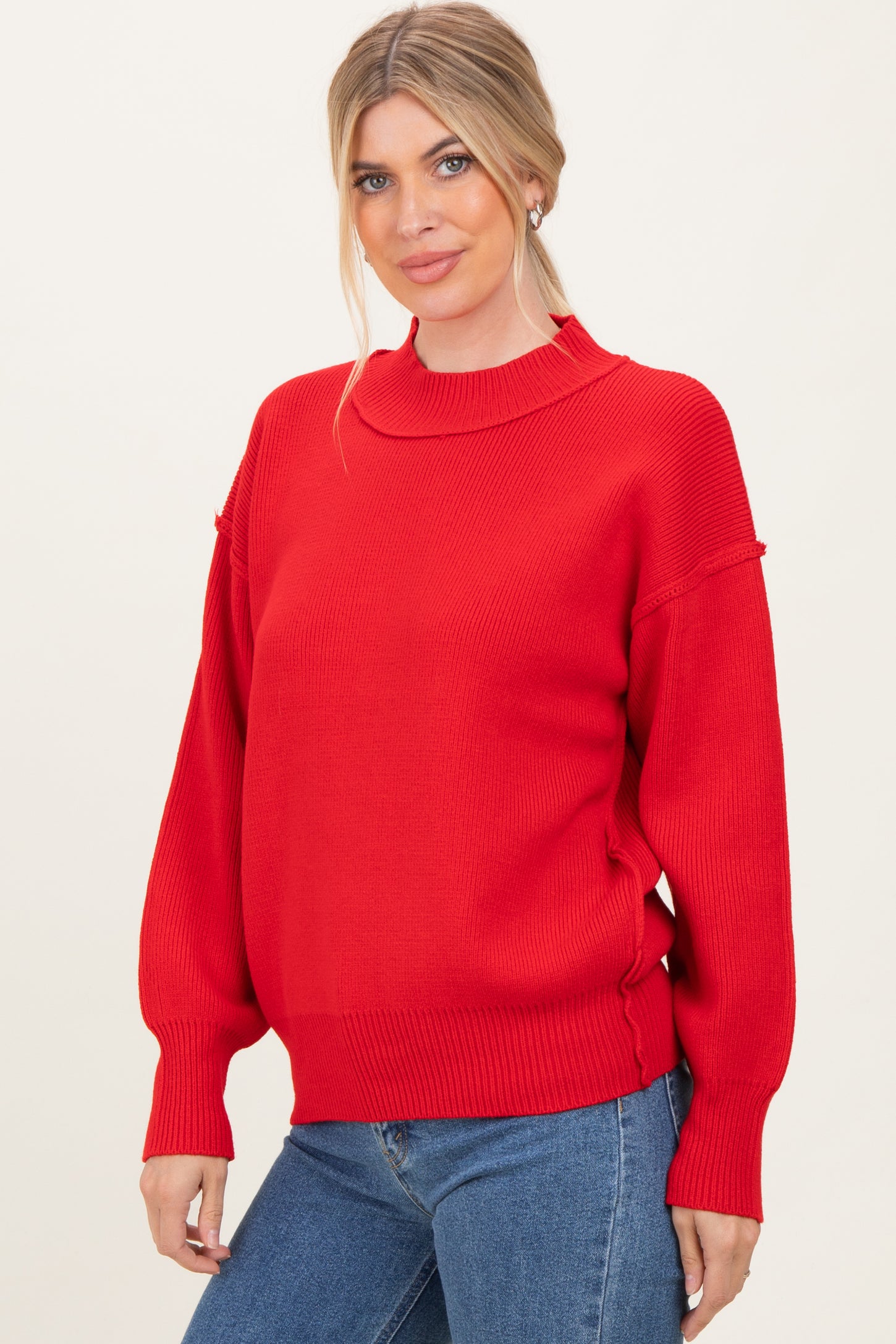 woman wearing a red oversized knit sweater with a high neckline and ribbed cuffs, paired with blue jeans