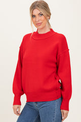 woman wearing a red oversized knit sweater with a high neckline and ribbed cuffs, paired with blue jeans