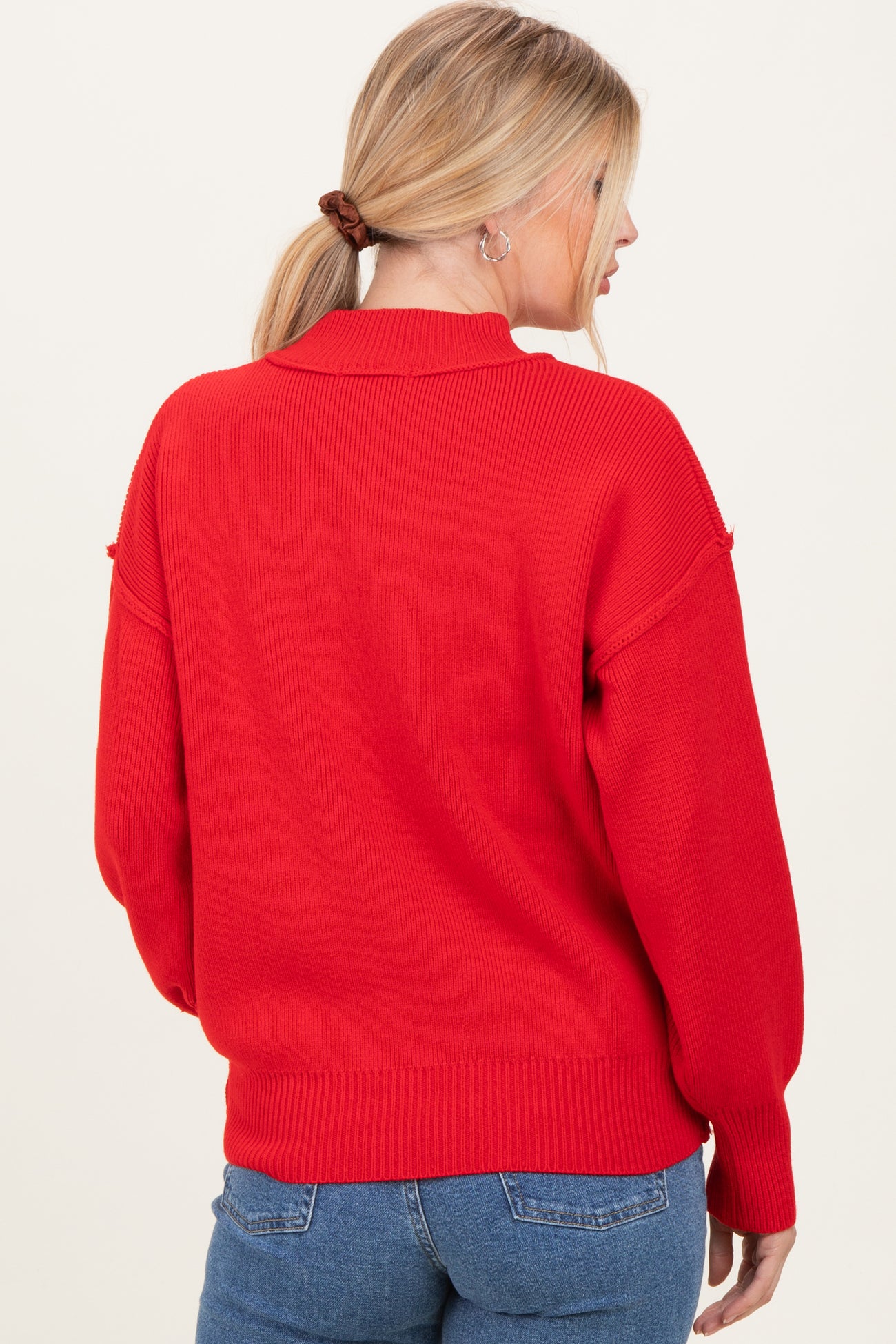 woman wearing a red oversized sweater, shown from the back, paired with blue jeans