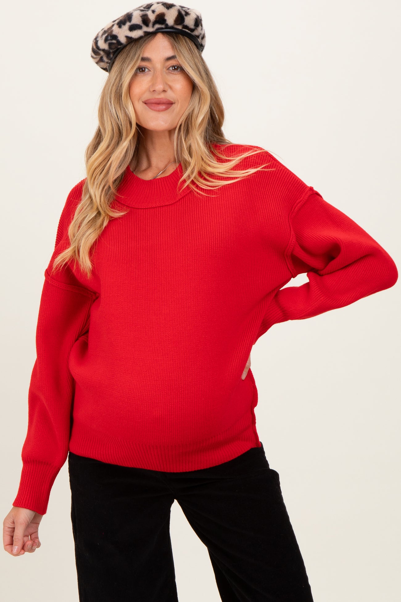 woman wearing a red oversized knit maternity sweater with a visible baby bump and a leopard print beret