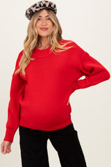 woman wearing a red oversized knit maternity sweater with a visible baby bump and a leopard print beret