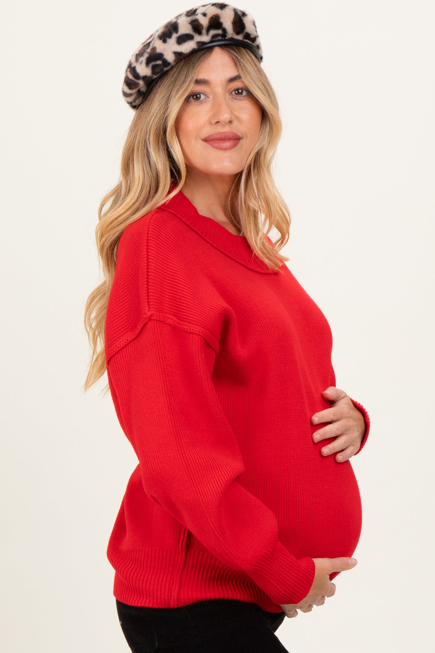 woman wearing a bright red maternity sweater and holding her baby bump, styled with a leopard print beret