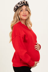 woman wearing a bright red maternity sweater and holding her baby bump, styled with a leopard print beret