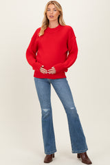 woman wearing a red oversized maternity sweater and blue flared jeans, holding her baby bump