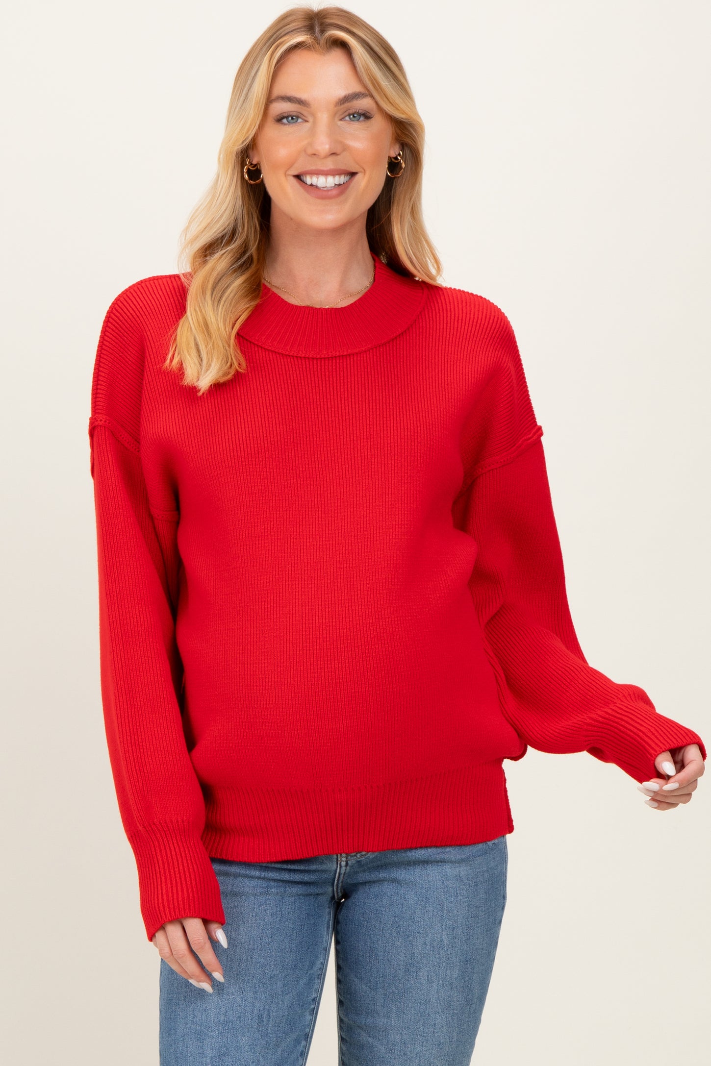 woman wearing a bright red oversized maternity sweater with ribbed texture and long sleeves, showing her baby bump