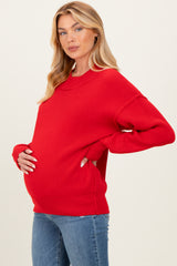 woman wearing a red oversized maternity sweater and holding her baby bump, paired with blue jeans