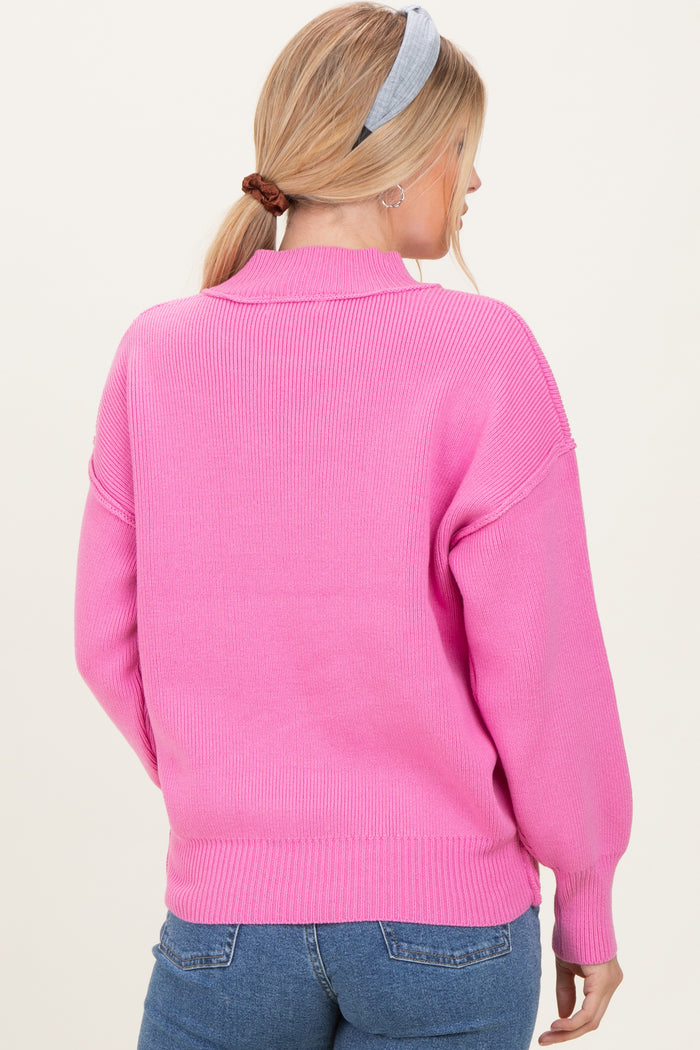 woman wearing a bright pink oversized knit sweater, showing the back and brushed hair in a ponytail