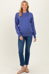 woman wearing a purple oversized maternity sweater with long sleeves and blue jeans, showing her baby bump