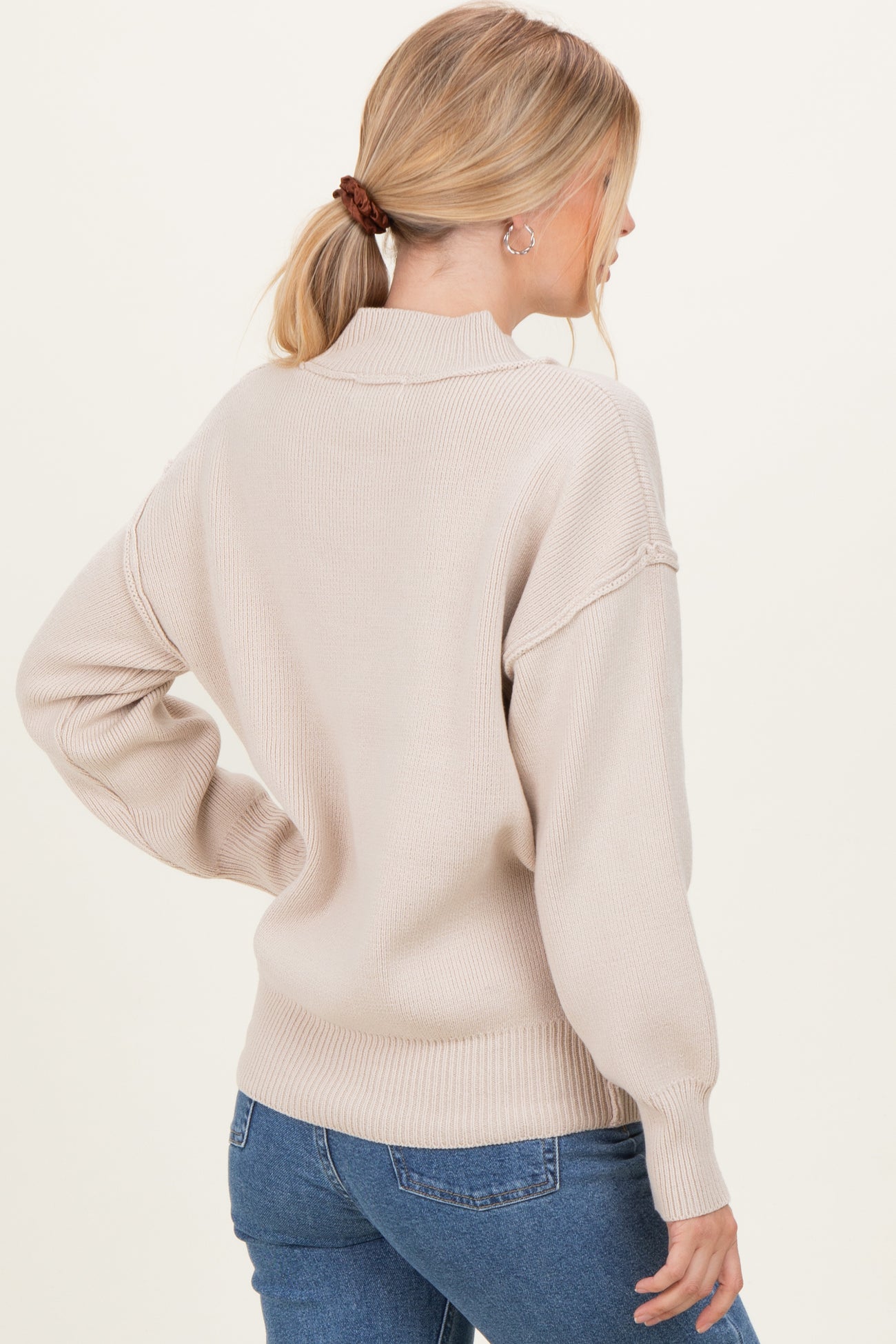 woman wearing a light beige oversized sweater with a high neck and balloon sleeves, styled with blue jeans