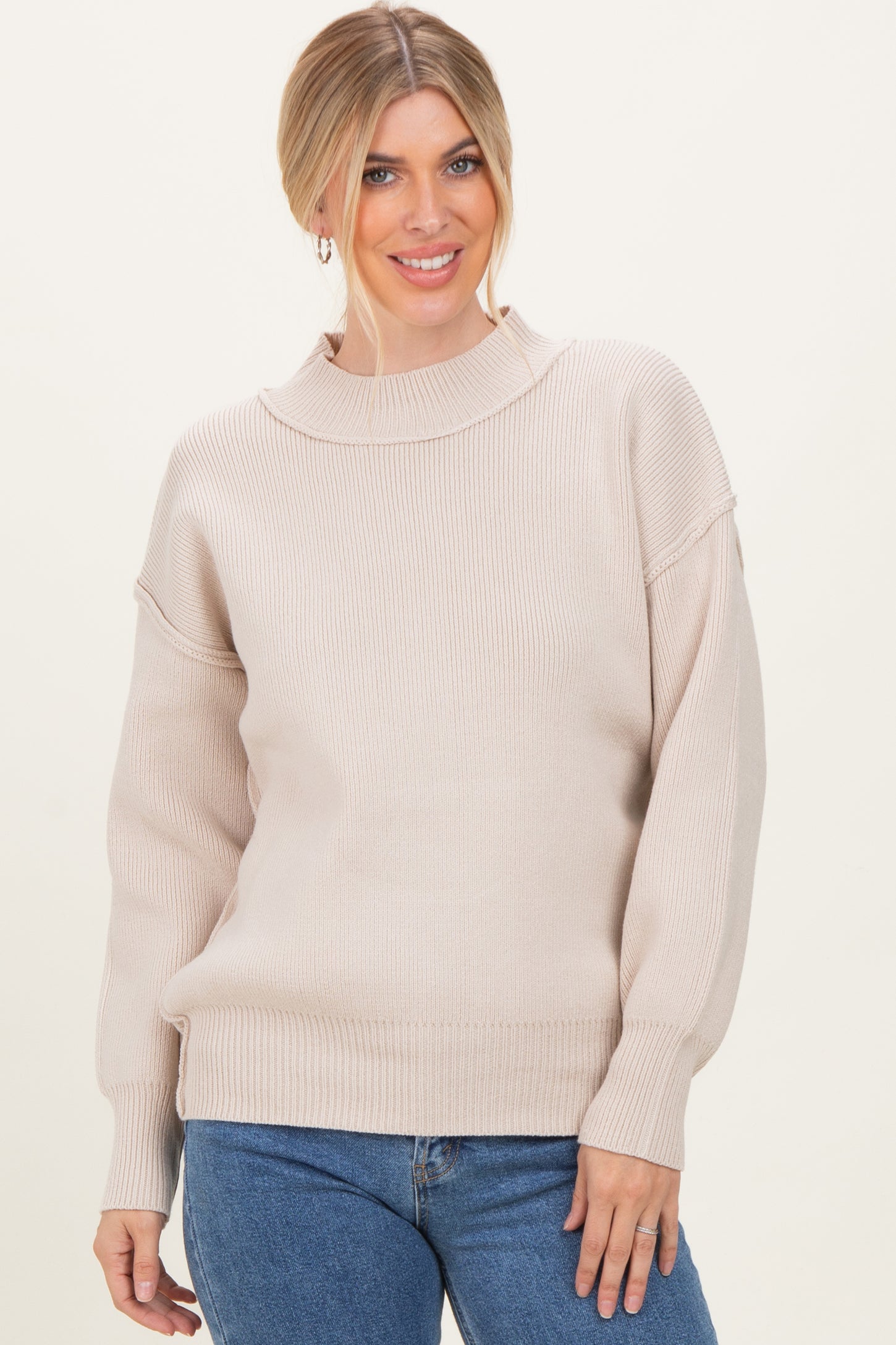 woman wearing a beige ribbed sweater with a high neckline and relaxed fit, paired with blue jeans