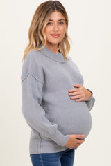 woman wearing a grey maternity sweater with a rounded neckline and holding her baby bump