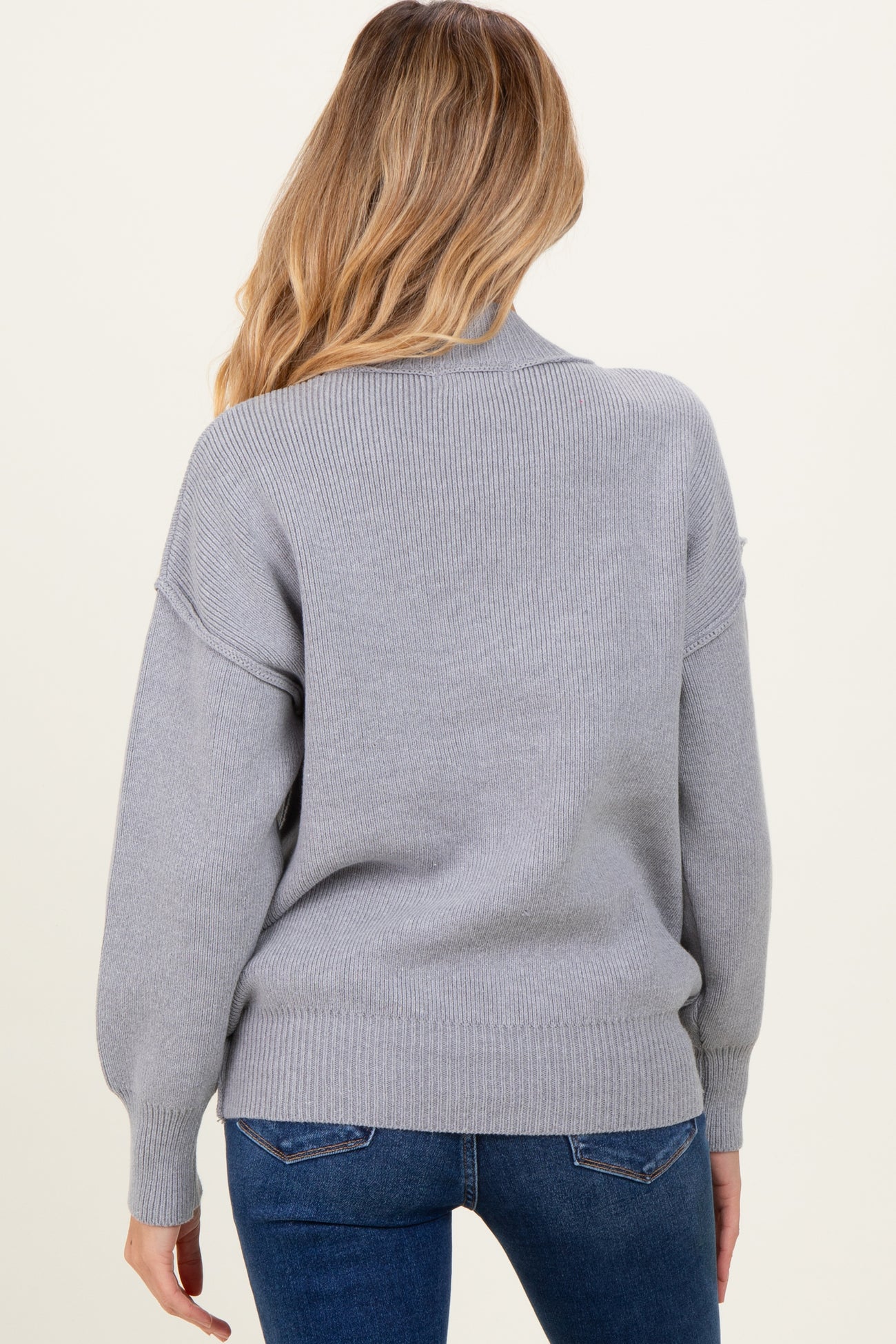woman wearing a grey oversized maternity sweater with a relaxed fit and ribbed detailing, facing away from the camera