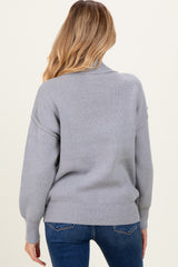 woman wearing a grey oversized maternity sweater with a relaxed fit and ribbed detailing, facing away from the camera