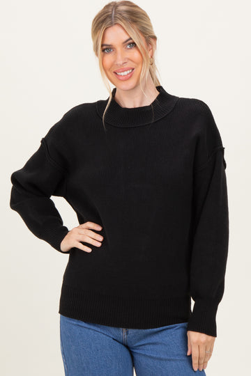 woman wearing a black knitted sweater with a relaxed fit and high neck, paired with blue jeans