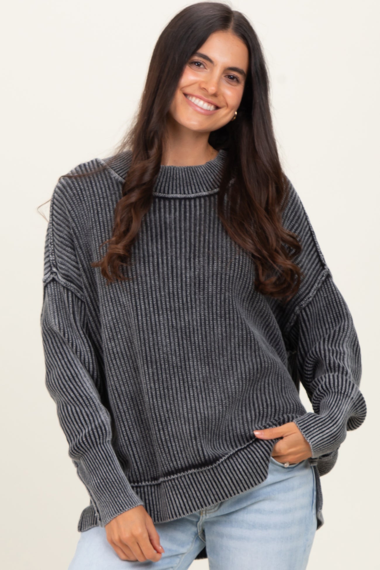 woman wearing a gray striped oversized sweater with a high neckline and dropped shoulders, smiling at the camera