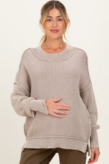 woman wearing a light beige oversized maternity sweater with ribbed detailing and holding her baby bump