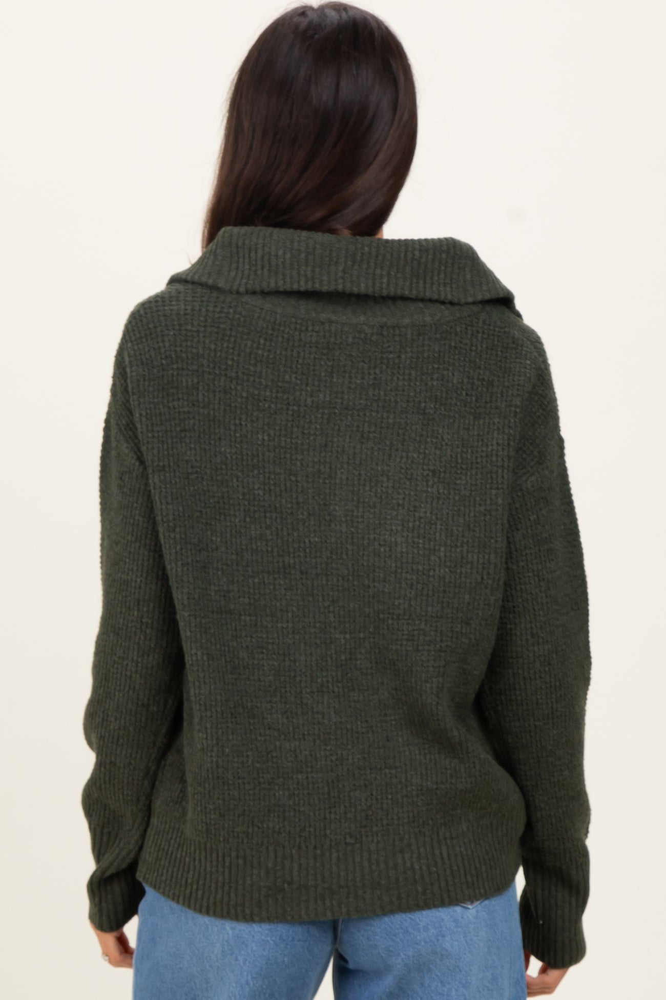 woman wearing an olive green oversized ribbed sweater with a wide collar, viewed from the back