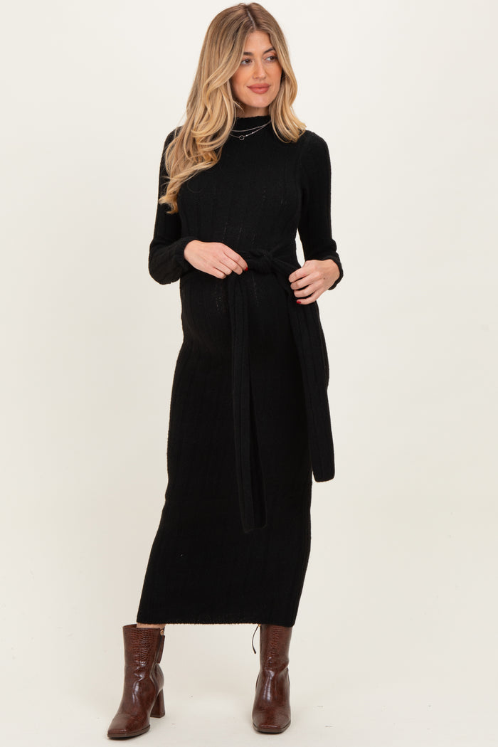 woman wearing a black knitted maternity dress with a tie waist detail and long sleeves, showing her baby bump