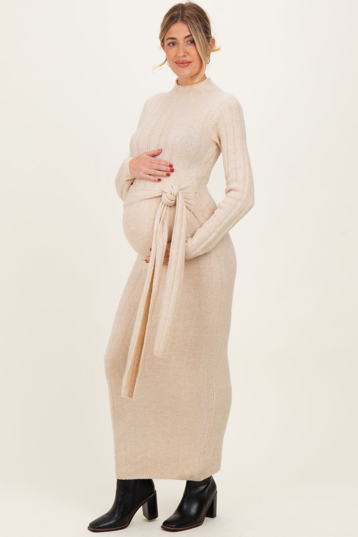 woman wearing a beige ribbed knit maternity dress with a tie at the waist and showing her baby bump