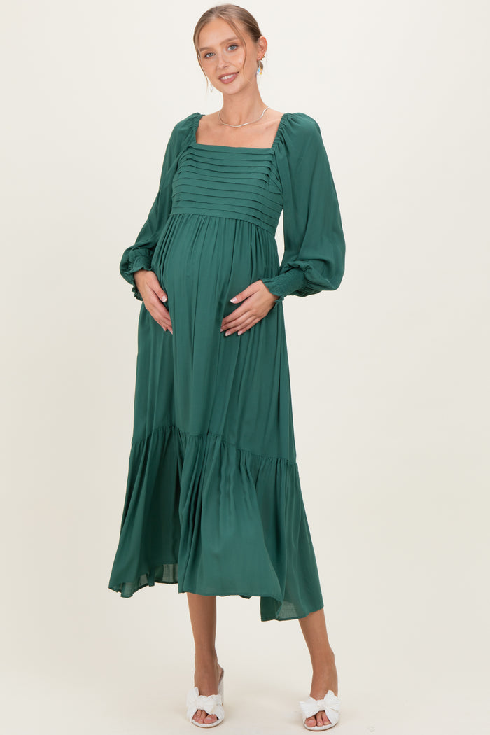 woman wearing a green maternity dress with a square neckline and balloon sleeves, holding her baby bump