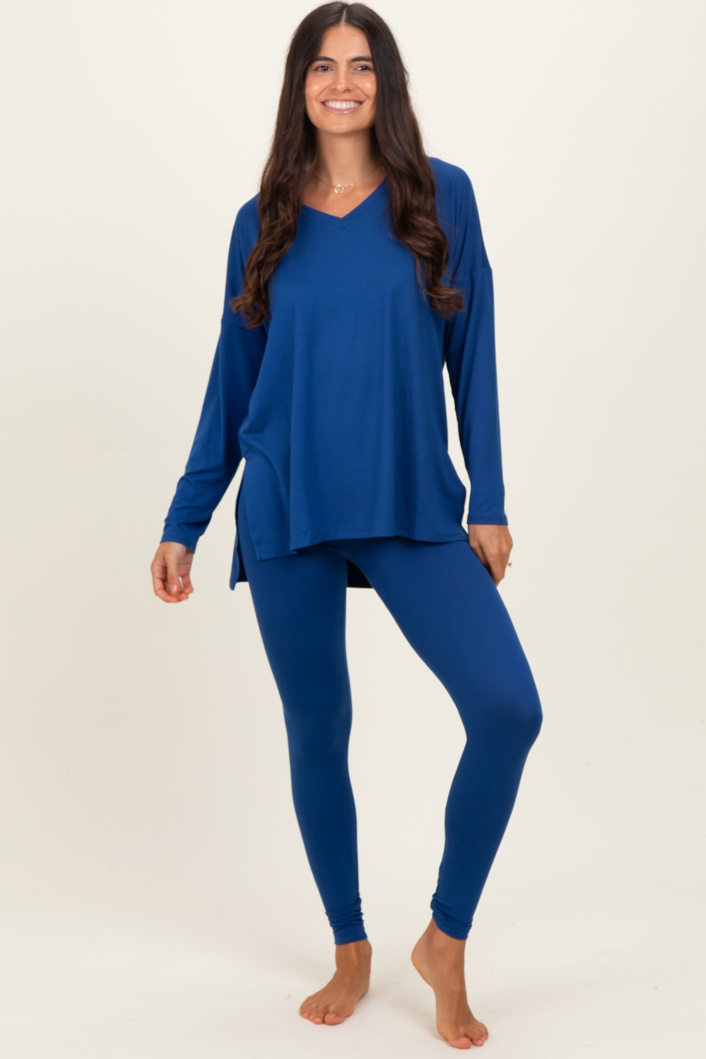 woman wearing a blue long sleeve loose fit top and matching leggings, standing barefoot against a plain background