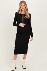 woman wearing a black ribbed maternity dress with long sleeves and sheer panel, holding her baby bump