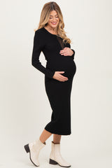 woman wearing a black ribbed maternity dress and cradling her baby bump, paired with white ankle boots