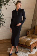 woman wearing a black maternity dress with denim collar and buttons, showing her baby bump while standing near a couch