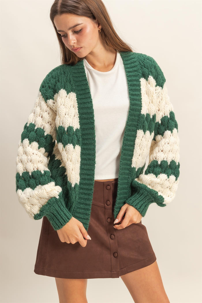 woman wearing a green and cream oversized knitted cardigan over a white top and a brown button-up mini skirt