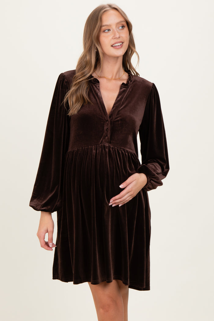 woman wearing a chocolate brown velvet maternity dress with long sleeves and a button-down neckline, holding her baby bump