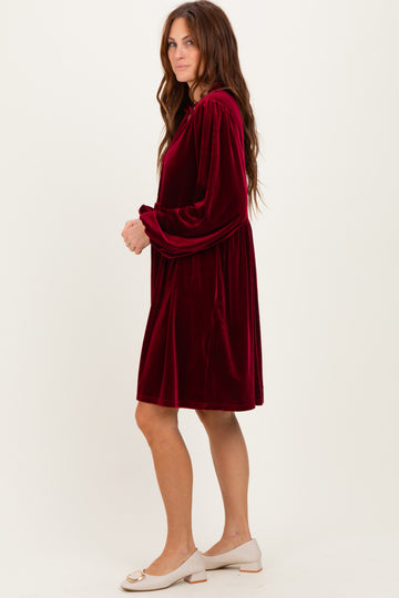 woman wearing a burgundy velvet long sleeve dress with a cinched waist and a relaxed fit