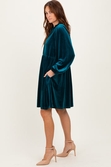 woman wearing a teal velvet long sleeve dress with pockets and a cinched waist, styled with nude heels