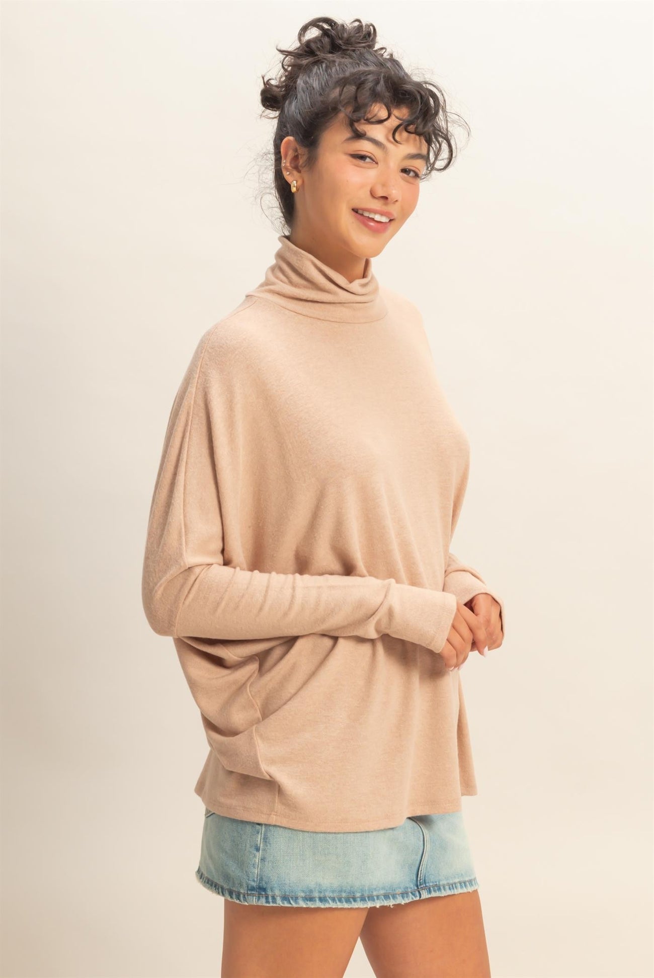 woman wearing a beige turtleneck sweater with a relaxed fit and blue denim shorts
