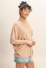 woman wearing a beige turtleneck sweater with a relaxed fit and blue denim shorts