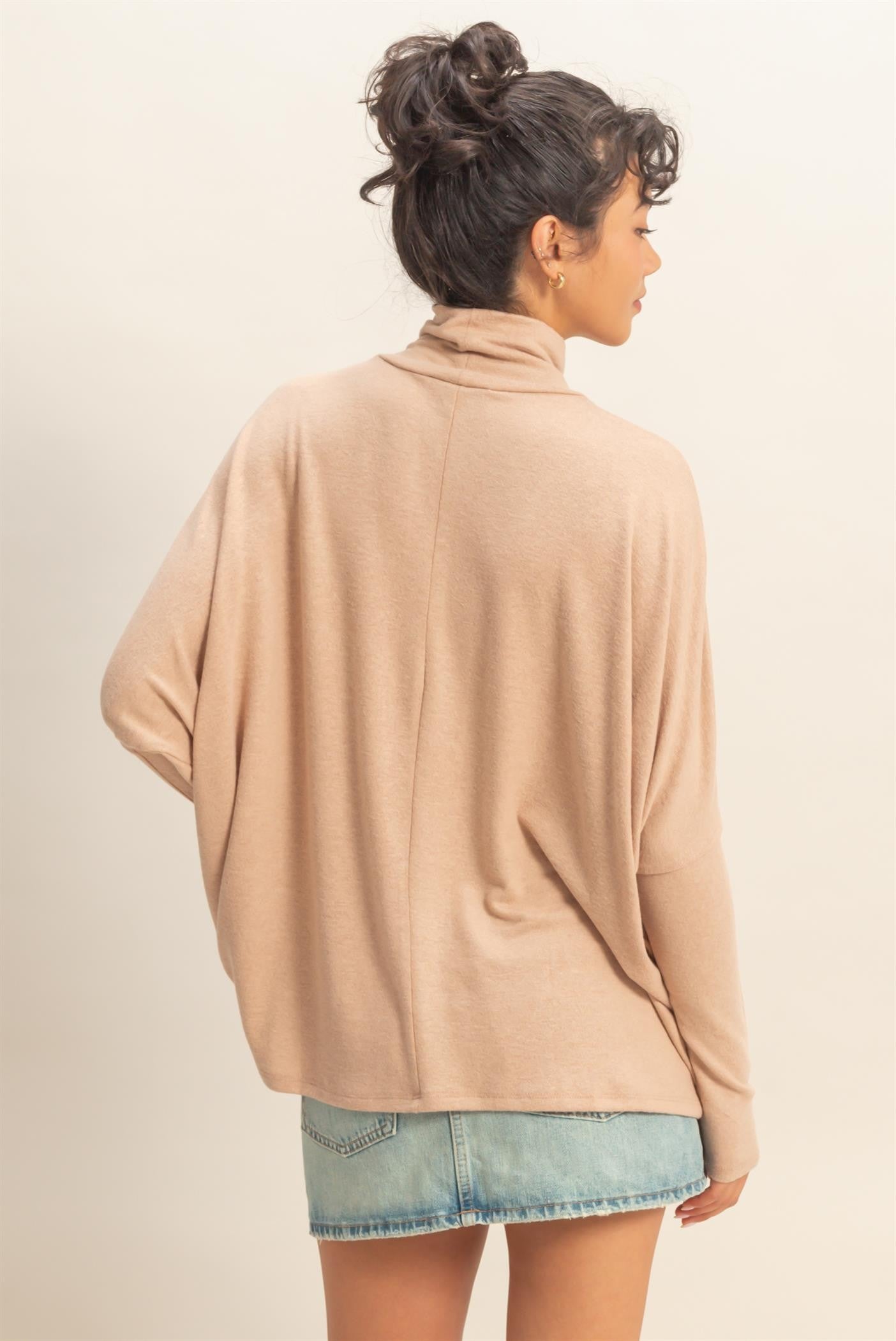 woman wearing a beige oversized turtleneck sweater paired with denim shorts, viewed from the back