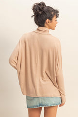 woman wearing a beige oversized turtleneck sweater paired with denim shorts, viewed from the back