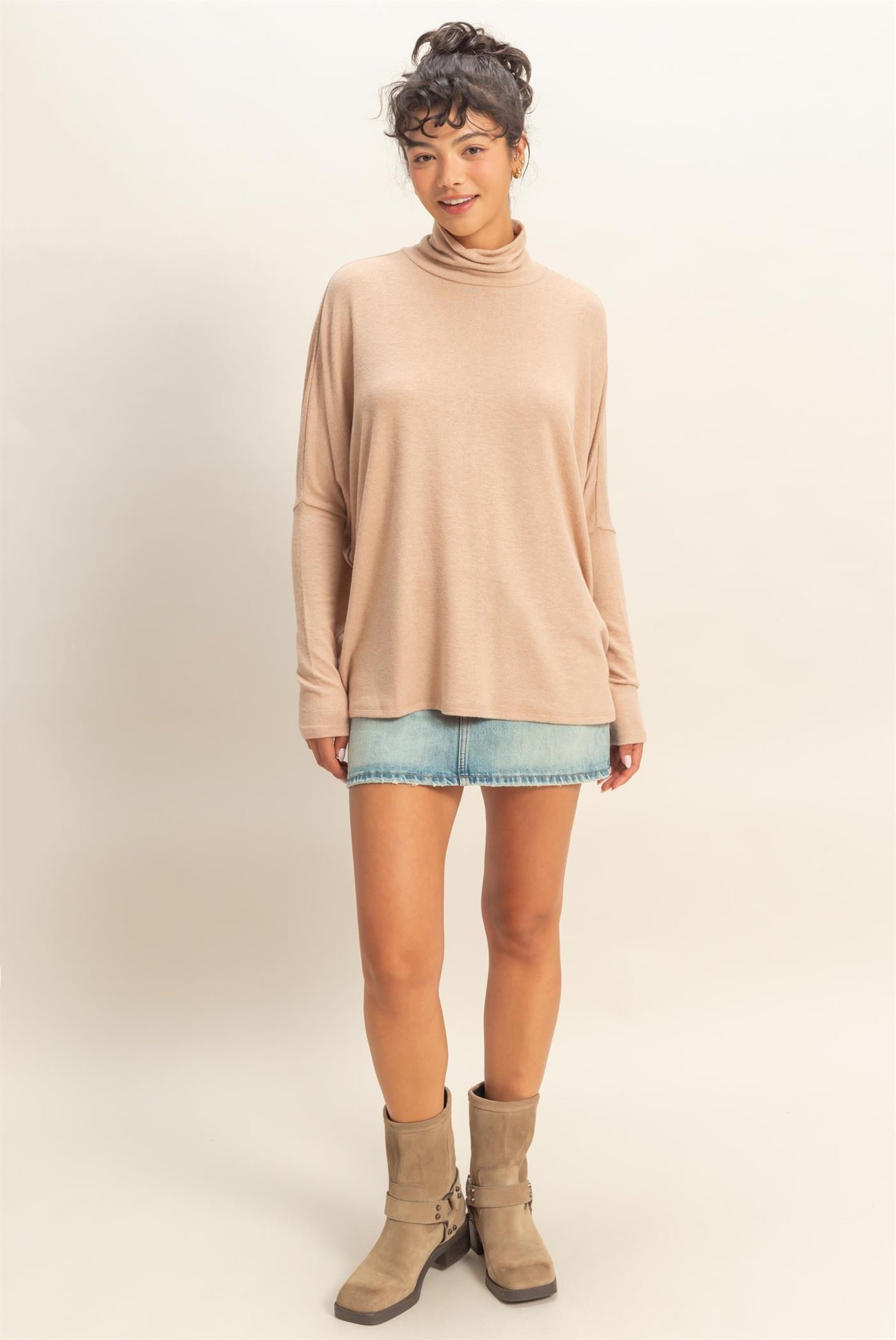 woman wearing a beige long sleeve turtleneck top with rolled cuffs and a denim mini skirt, paired with knee-high boots
