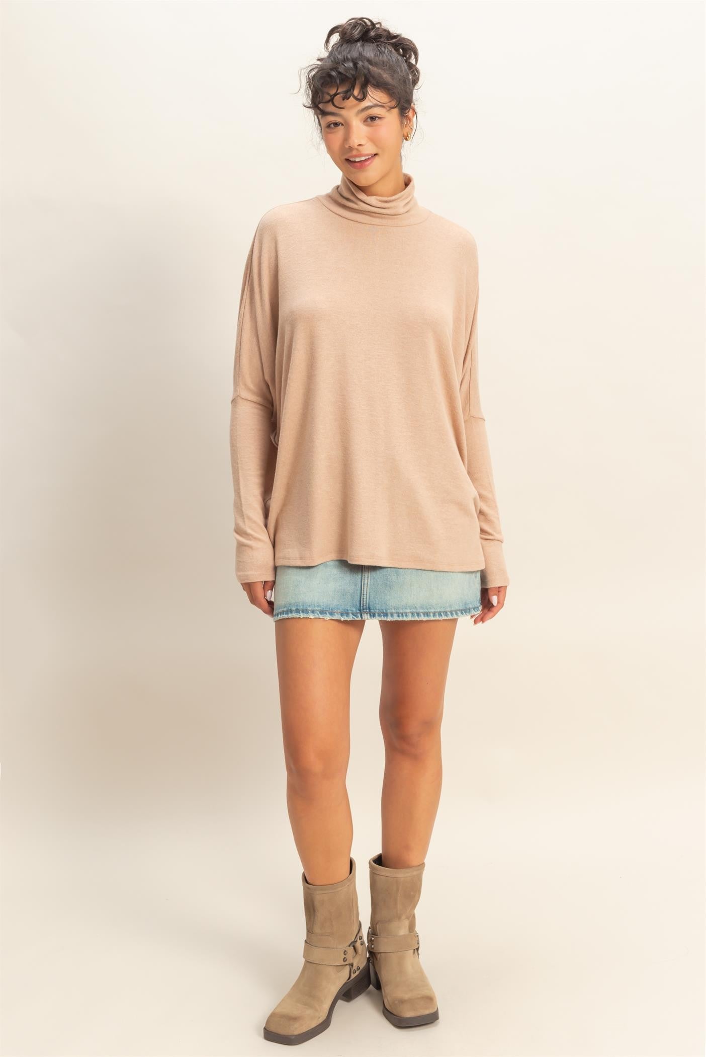 woman wearing a beige long sleeve turtleneck top with rolled cuffs and a denim mini skirt, paired with knee-high boots