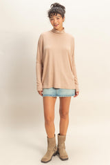 woman wearing a beige long sleeve turtleneck top with rolled cuffs and a denim mini skirt, paired with knee-high boots