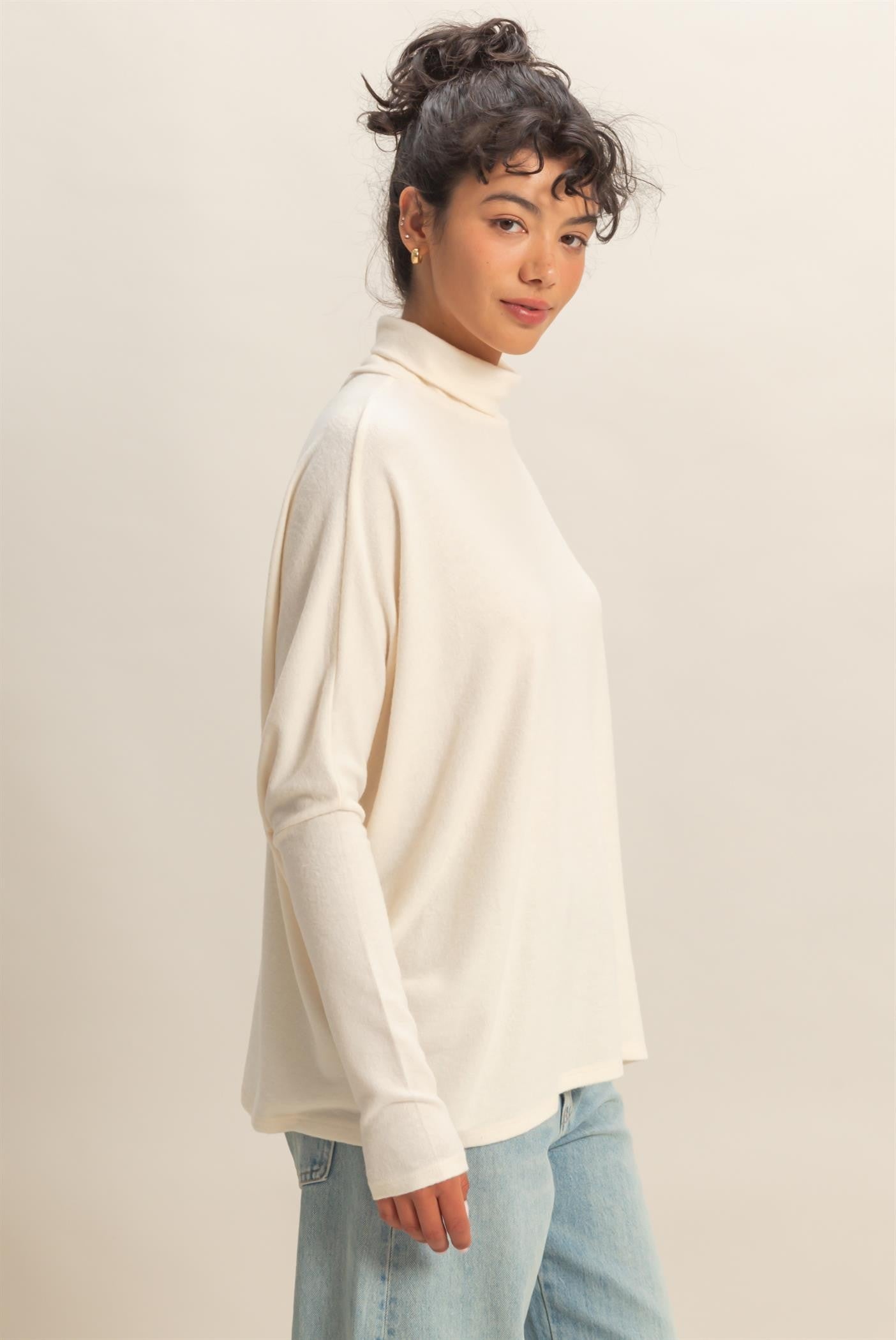 woman wearing a cream long sleeve turtleneck top with relaxed fit and light blue jeans