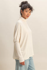 woman wearing a cream long sleeve turtleneck top with relaxed fit and light blue jeans