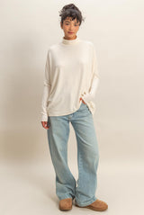 woman wearing a cream long sleeve oversized turtleneck sweater and light blue wide-leg jeans