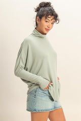 woman wearing a light green oversized turtleneck sweater with long sleeves and front pockets, paired with a denim mini skirt