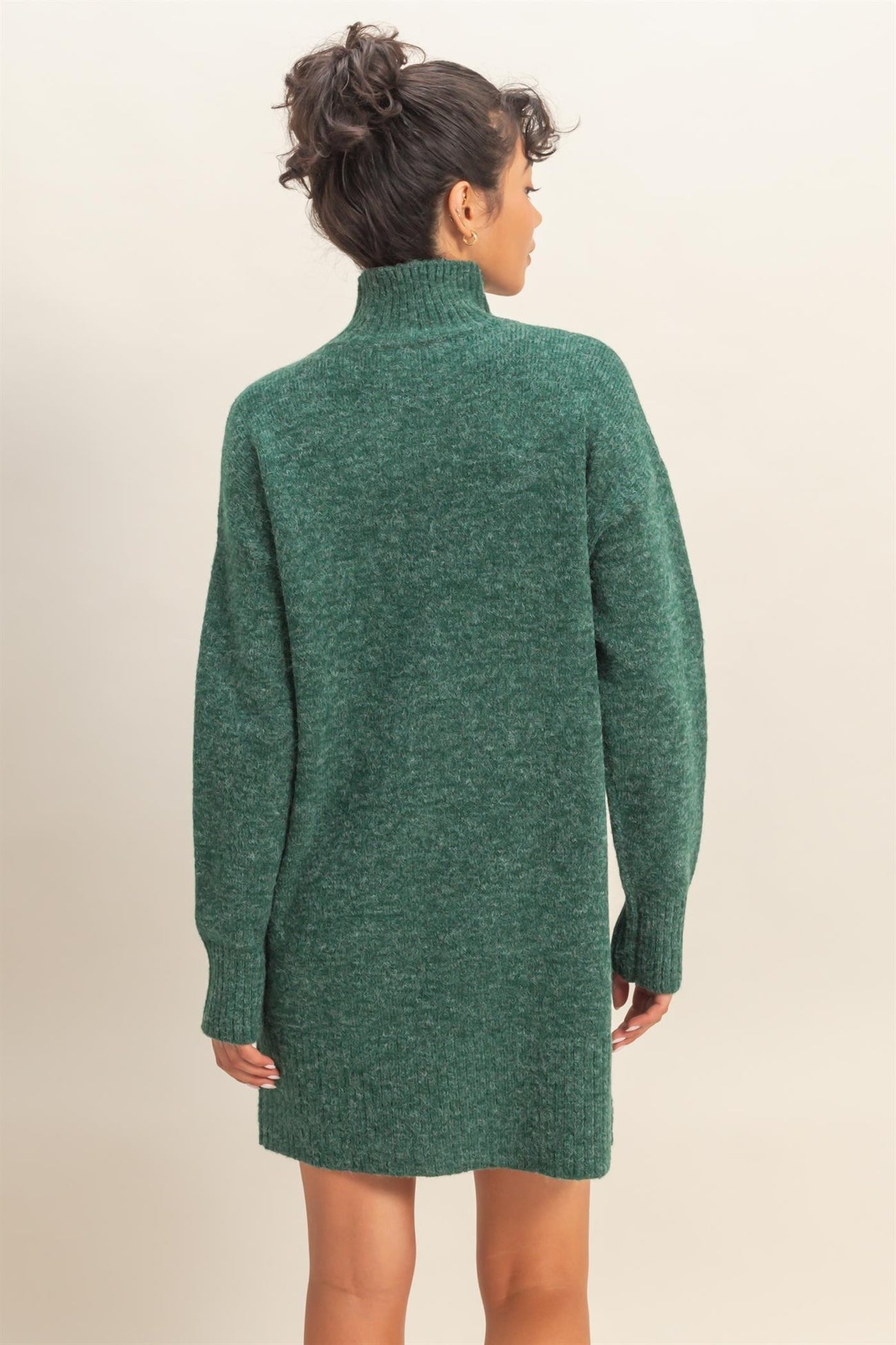 woman wearing a green oversized sweater dress with a high collar and long sleeves, viewed from the back